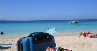 a person's foot on a beach with a suitcase