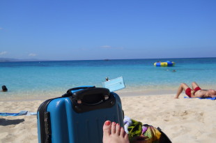 a person's foot on a beach with a suitcase