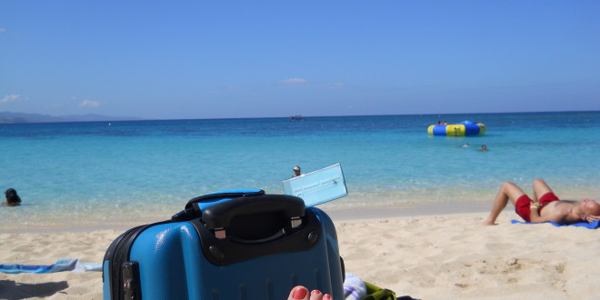 a person's foot on a beach with a suitcase