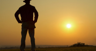 a man standing in a field with the sun in the background