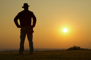 a man standing in a field with the sun in the background