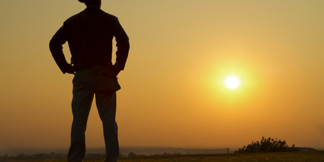 a man standing in a field with the sun in the background