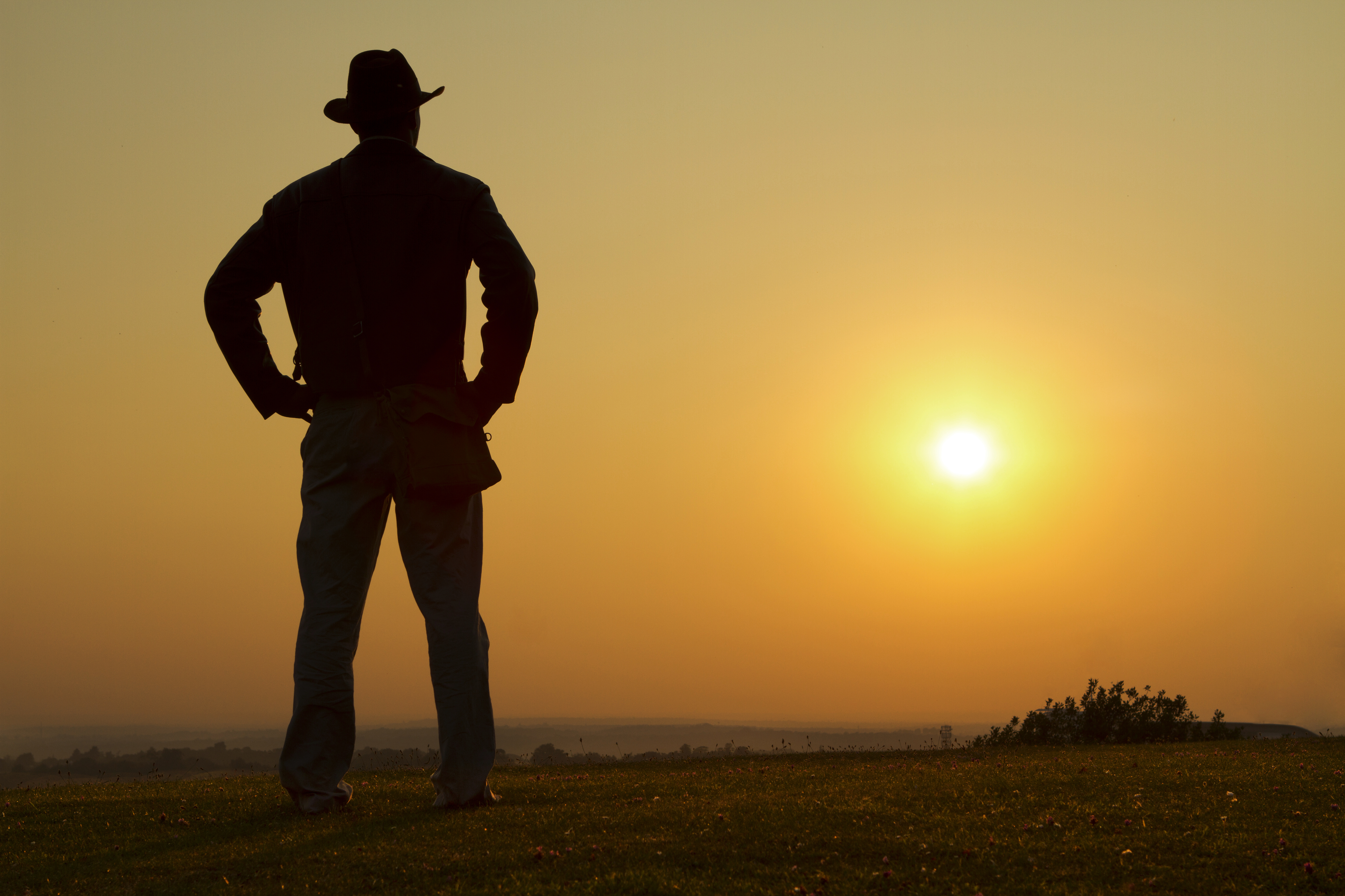a man standing in a field with the sun in the background