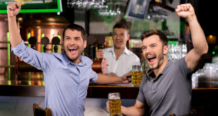 a group of men sitting at a bar holding beer glasses