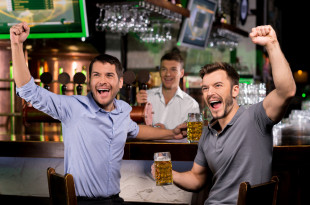 a group of men sitting at a bar holding beer glasses