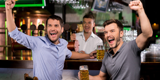 a group of men sitting at a bar holding beer glasses