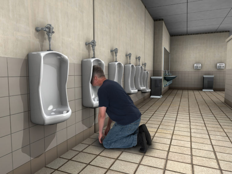 a man kneeling on the floor in a bathroom with urinals