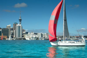 a sailboat with a red sail in the water with a city in the background