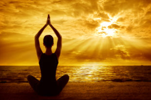 a woman sitting on the beach with her hands together