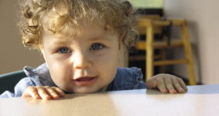 a baby with curly hair looking over a table