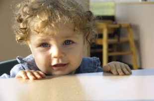 a baby with curly hair looking over a table