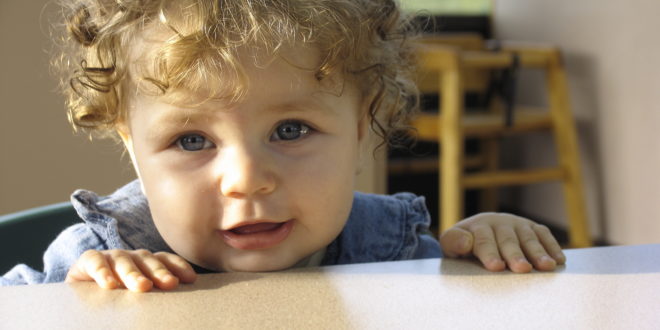 a baby with curly hair looking over a table