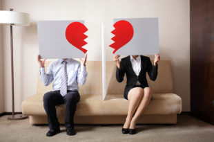 a man and woman sitting on a couch holding up a sign