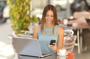 a woman sitting at a table with a laptop and a phone