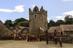 a stone tower with a clock tower and farm equipment