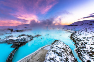 a blue water with snow and a pink sky