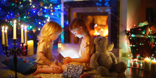 two girls opening a gift box in front of a fireplace