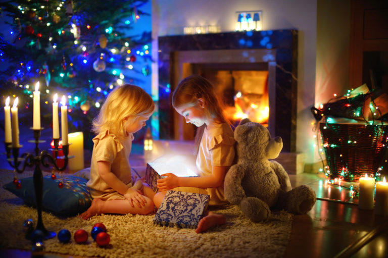 two girls opening a gift box in front of a fireplace